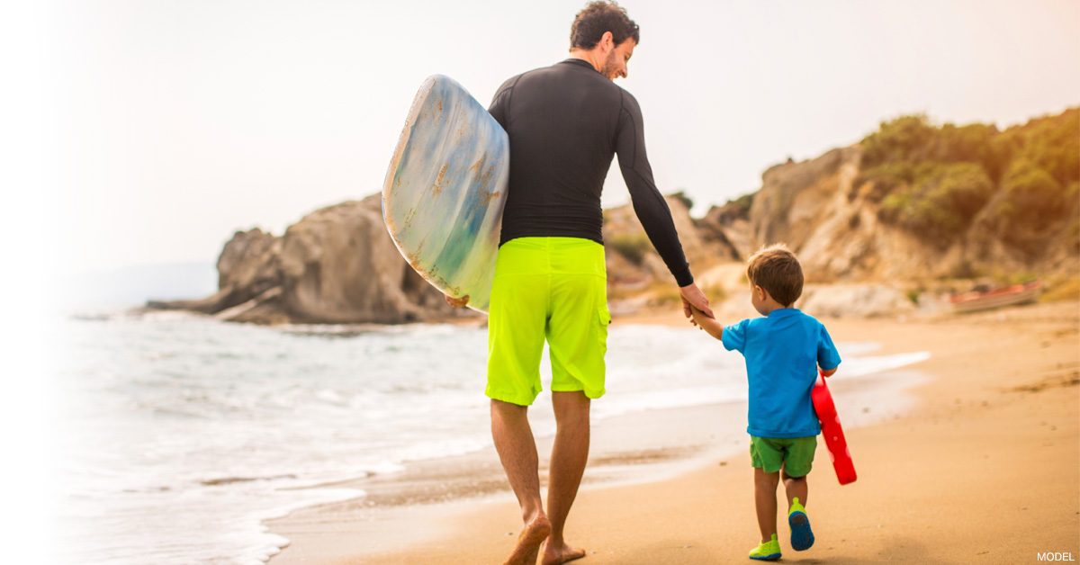 Slim dad walking on the beach with his son.