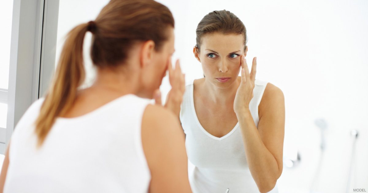 Woman looking in mirror after applying skincare products.