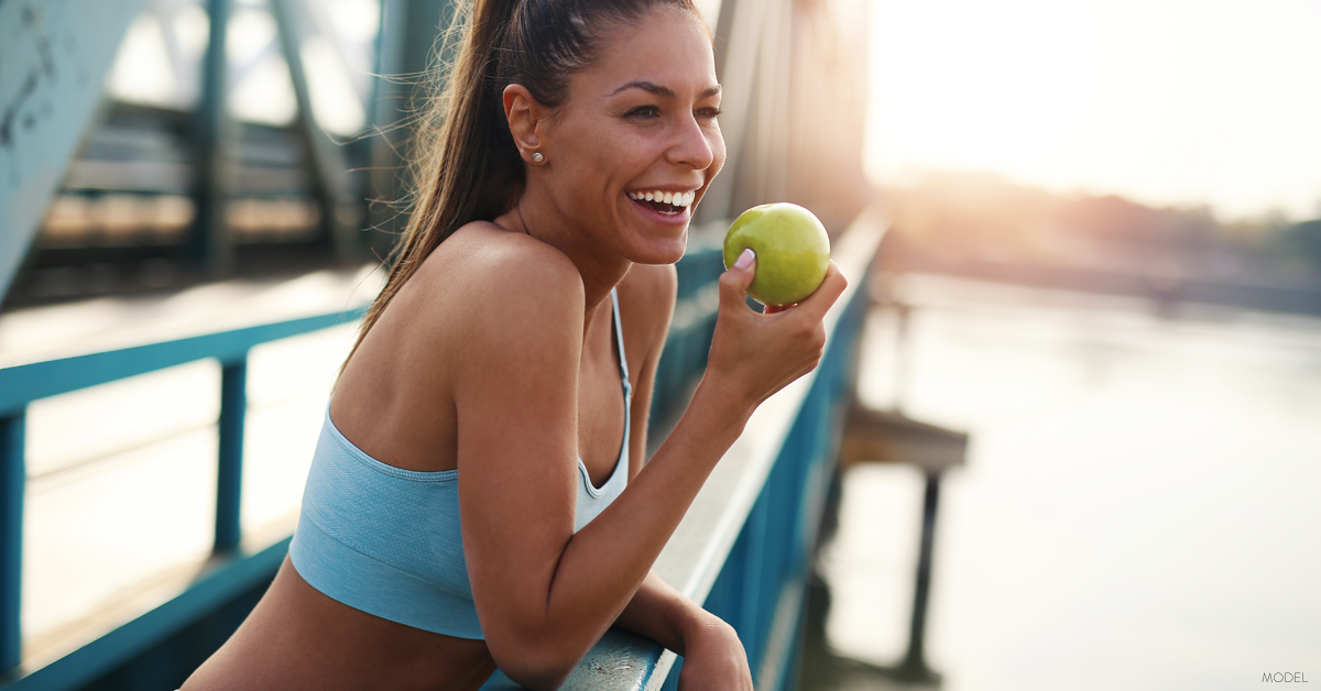 Athletic woman in workout attire smiling and eating apple