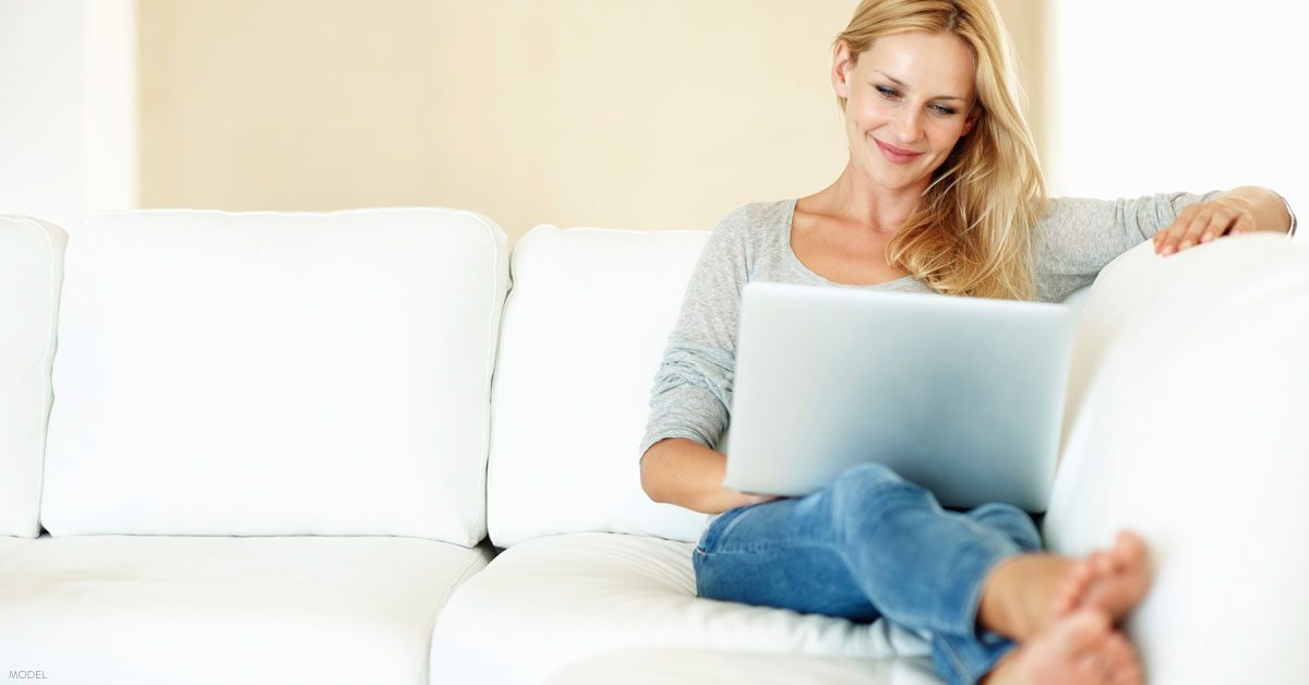 Woman sitting on couch researching tummy tuck surgery on her laptop