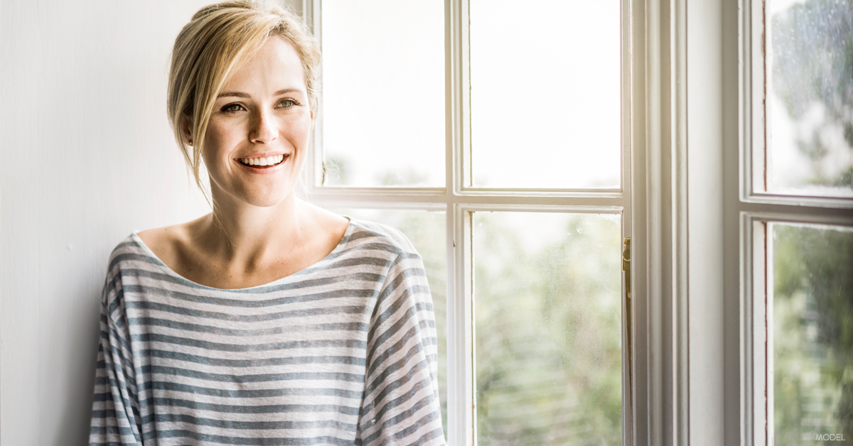 Blonde woman smiling standing next to window