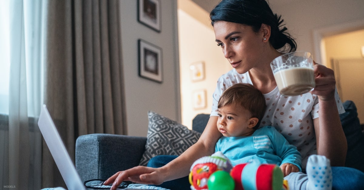 Woman holding son and coffee while researching mommy makeover online (MODELS)