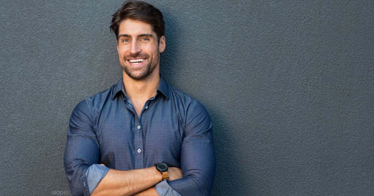 Attractive man leaning against a wall with his arms crossed and smiling (model)