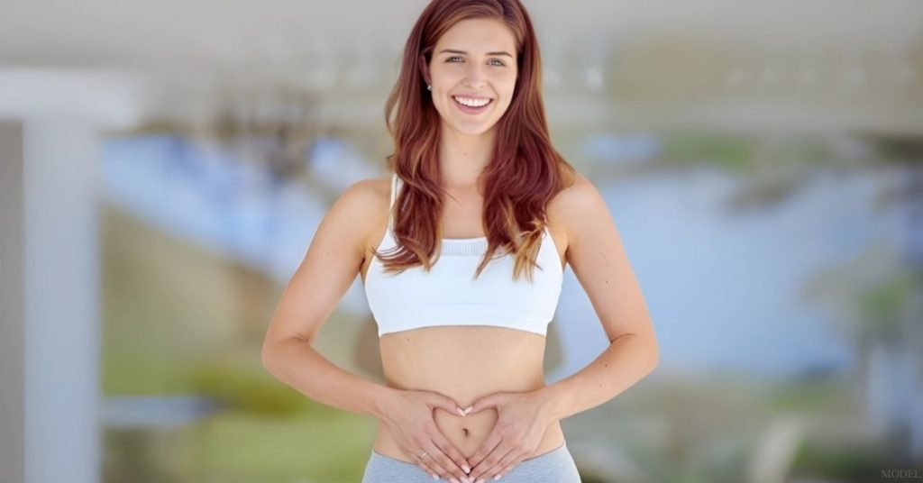 Woman forming a heart shape with her hands on her abdomen to showcase tummy tuck results (model)