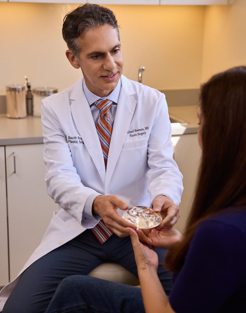 Dr. Michael Newman handing a breast implant sample to a patient during a consultation.